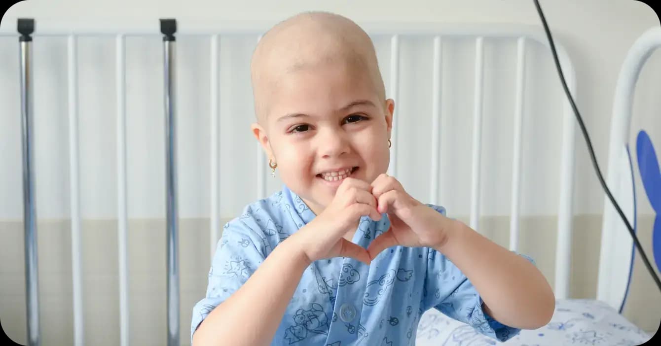 Menina com câncer fazendo gesto de coração com a mão