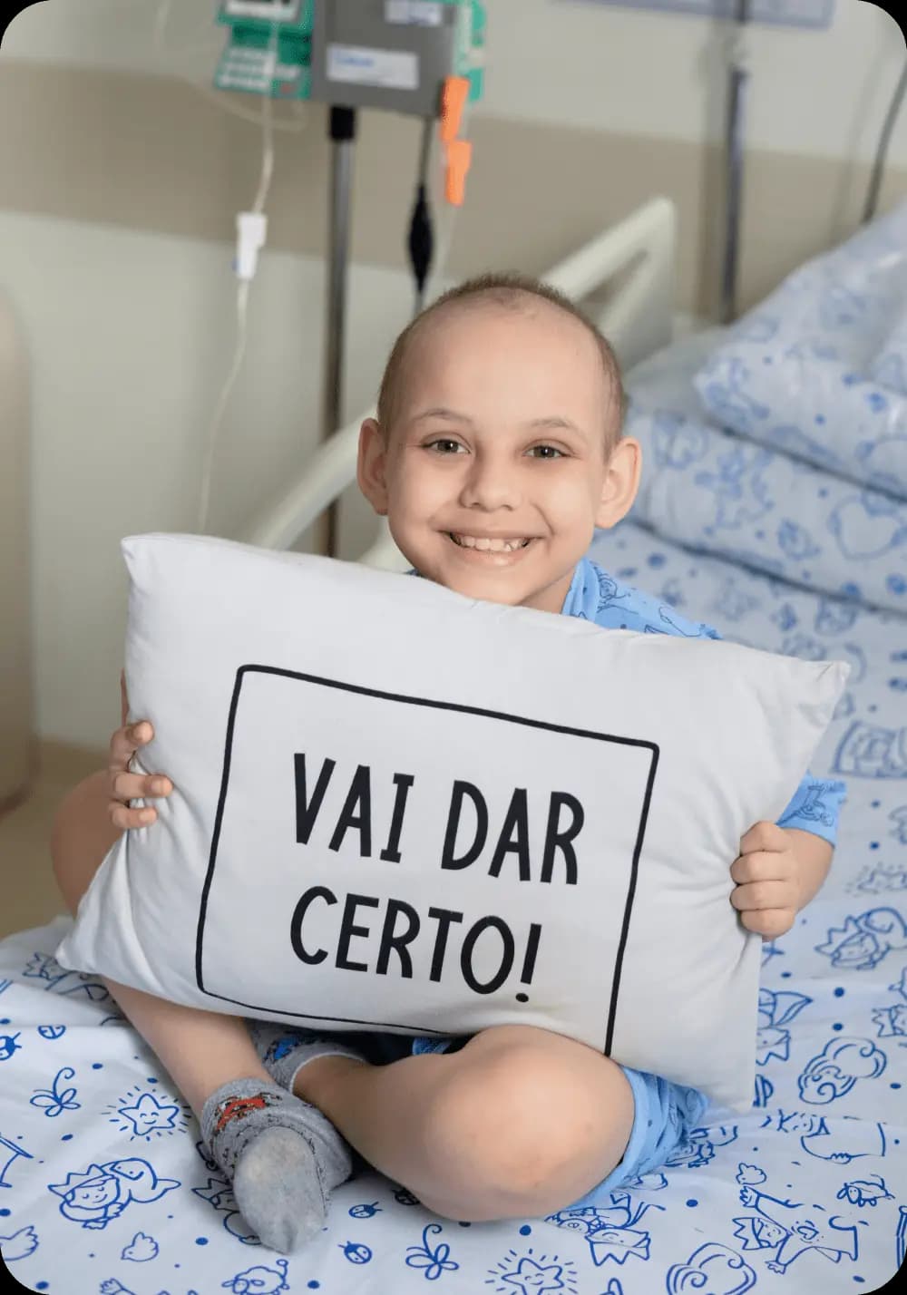 Criança em tratamento segurando um travesseiro que está escrito: "Vai dar certo!"